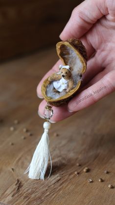 someone is holding a tiny stuffed animal in an open shell with a tassel hanging from it