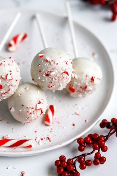 three white cake pops on a plate with candy canes and sprinkles