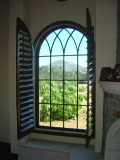 an arched window with shutters open in front of a fireplace and view of mountains