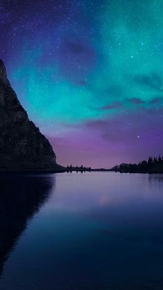 the night sky is filled with stars and aurora lights over a body of water in front of a mountain