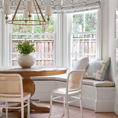 a dining room table with chairs and a bench in front of two windows that look out onto the backyard