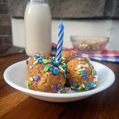 three cookies with sprinkles and a candle are on a plate next to a glass of milk