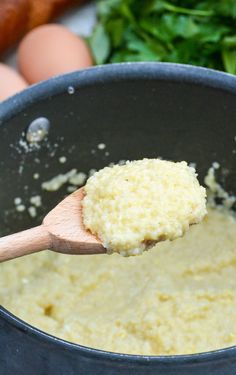 a wooden spoon is stirring some food in a pot with eggs and spinach on the side