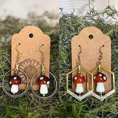 two pairs of earrings with red and white mushrooms on them sitting in grass next to each other