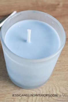 a small white candle sitting in a glass container with a spoon on the table next to it