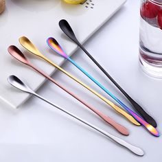 stainless steel spoons with colorful handles are on a white surface next to fruit and water