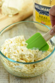 a person mixing food in a glass bowl with a green spatula and wooden spoon