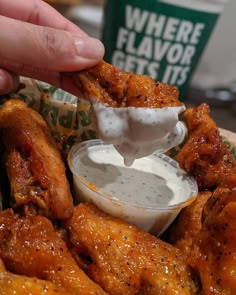 a person dipping sauce on some chicken wings