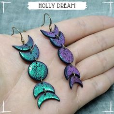 three purple and green earrings on a person's hand with the words holly dream written below them