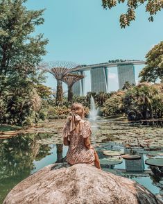 a woman sitting on top of a rock next to a pond