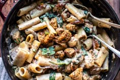 a skillet filled with pasta, meat and spinach on top of a wooden table