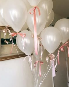 a bunch of white balloons with pink ribbons tied around them in front of a mirror