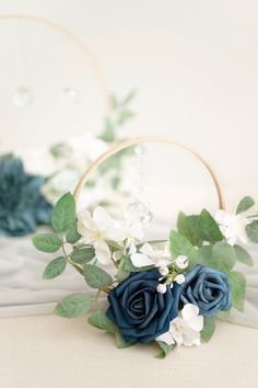 a blue rose and white flower arrangement in a hoop with greenery on the side