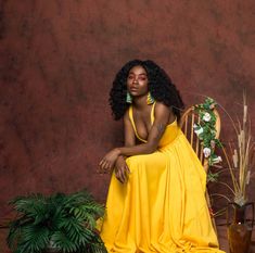 a woman in a yellow dress sitting on a chair next to some plants and flowers