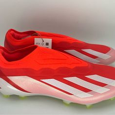 a pair of red and white soccer shoes with tags on the soles that say adidas