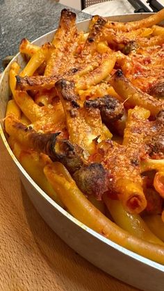 a pan filled with pasta and meat covered in sauce on top of a wooden table