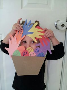 a young boy holding up a cardboard box with hand prints on it's face