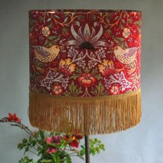 a red lamp shade with fringe trim and birds on it next to a potted plant