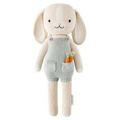 a stuffed animal with overalls and carrots on it's legs, sitting in front of a white background