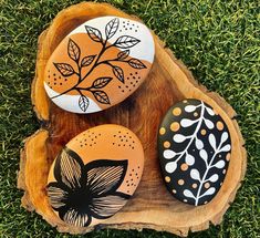 three painted rocks sitting on top of a piece of wood next to each other in the grass