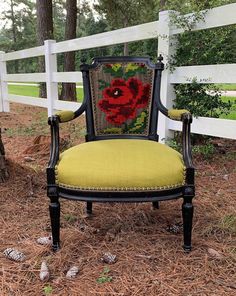 an old chair with a red flower on it sitting in front of a white fence