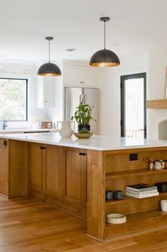 an open kitchen with wooden cabinets and white counter tops, along with black pendant lights hanging from the ceiling