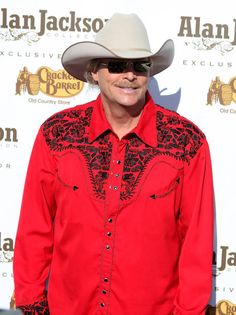 a man in a red shirt and cowboy hat posing for a photo on the red carpet