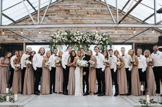 a group of people standing next to each other in front of a wooden structure with flowers and greenery