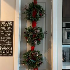 christmas wreaths hanging on the front door of a house decorated with evergreen, pine cones and red ribbon