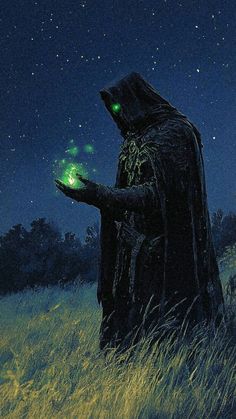 a man in a black robe holding a green light up item on his hand while standing in tall grass at night