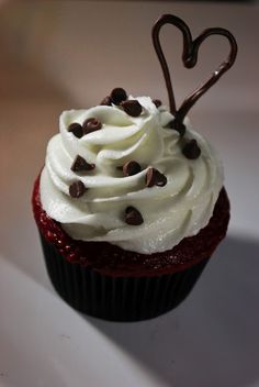 a cupcake with white frosting and chocolate chips in the shape of a heart