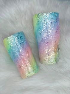 two rainbow colored glitter cups sitting on top of a white fur covered floor next to each other