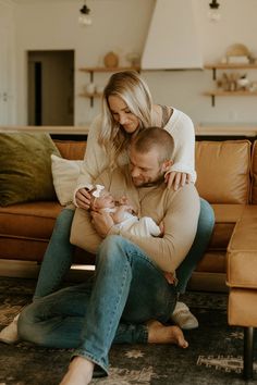 a man holding a baby while sitting on the floor next to a woman with her arm around him