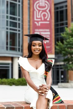 a woman wearing a graduation cap and gown sitting on a brick wall in front of a building