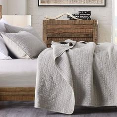 a bed with a blanket and pillows on top of it next to a wooden headboard