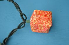 an orange origami cube sitting on top of a blue table next to a black cord