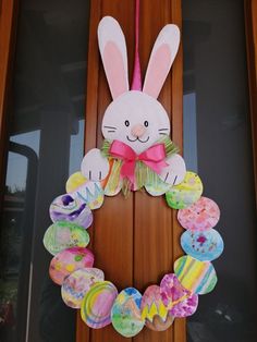 a wreath made out of paper with a bunny face on it and colorful eggs hanging from the front door