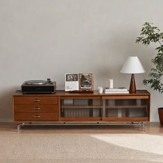 a record player sitting on top of a wooden cabinet next to a lamp and potted plant