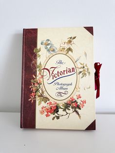 a book with an ornate cover and red ribbon on the front, sitting on a white surface