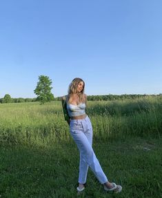 a woman standing in the middle of a field wearing white jeans and a crop top