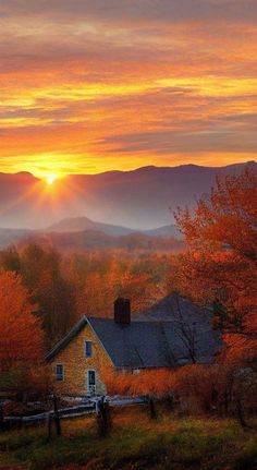 the sun is setting over a farm with mountains in the background and trees that are changing colors