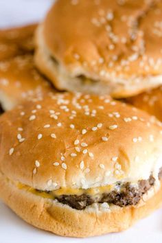 three hamburgers sitting on top of a white plate covered in cheese and sesame seeds