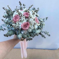 a bridal bouquet with pink roses and white flowers is held by someone's hand