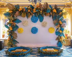 an elaborately decorated backdrop with blue and yellow flowers, leaves and other decorations on the wall