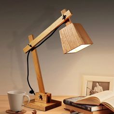 a wooden desk lamp sitting on top of a table next to an open book and coffee cup