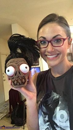 a woman holding up a creepy mask with eyes and hair on it's head