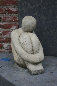 a stone statue sitting on top of a cement slab next to a brick wall and door