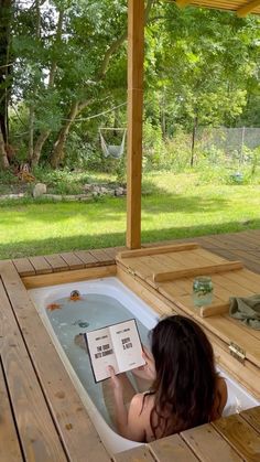 a woman sitting in a hot tub reading a book on top of the deck outside