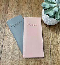 two notebooks sitting on top of a wooden table next to a potted plant