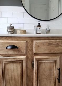 a bathroom vanity with wooden cabinets and a round mirror on the wall above it's sink